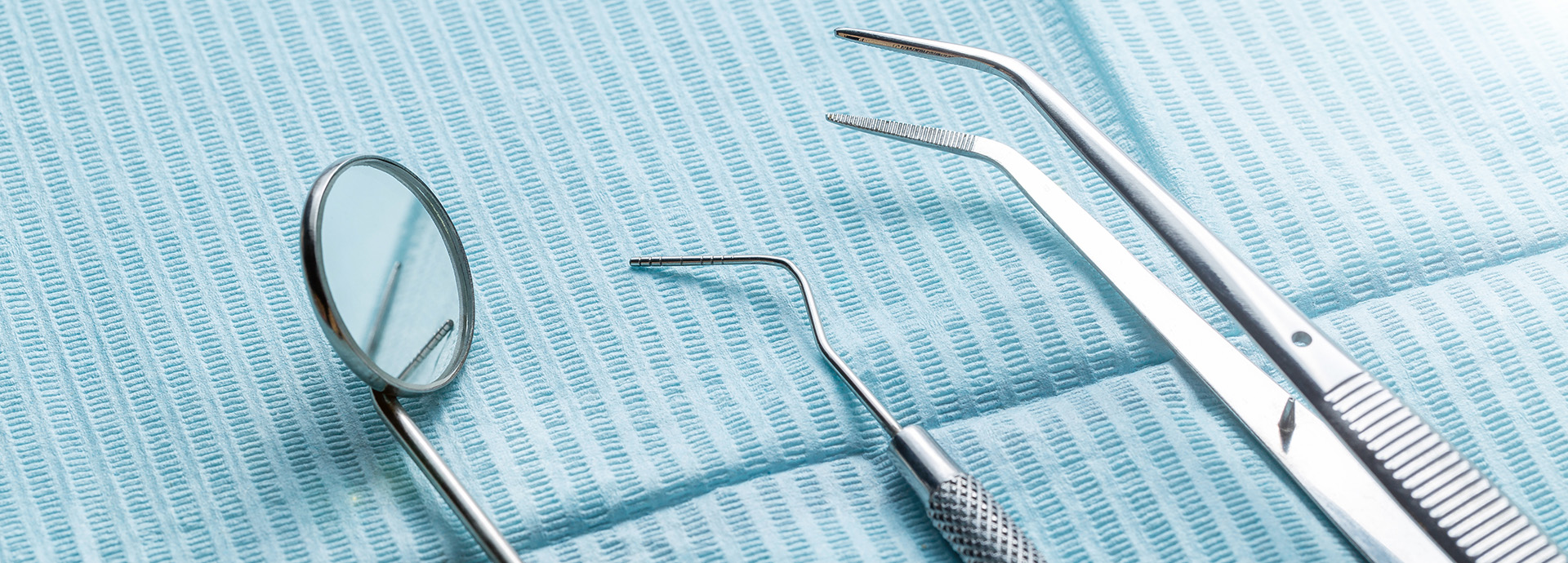 The image shows a collection of dental instruments, including a magnifying glass and various tools, arranged on a blue cloth surface.