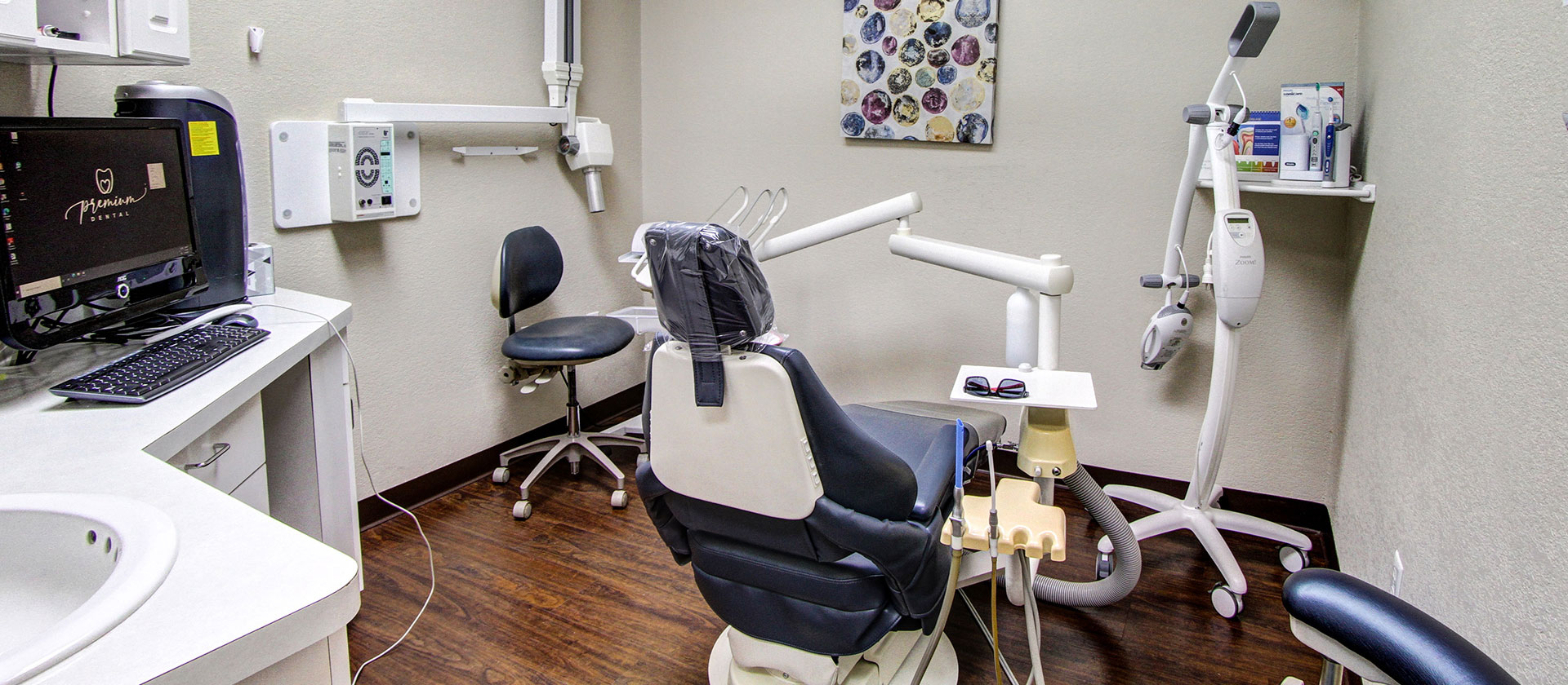 A person is seated in a dental chair, receiving care from a dental professional who stands behind them.