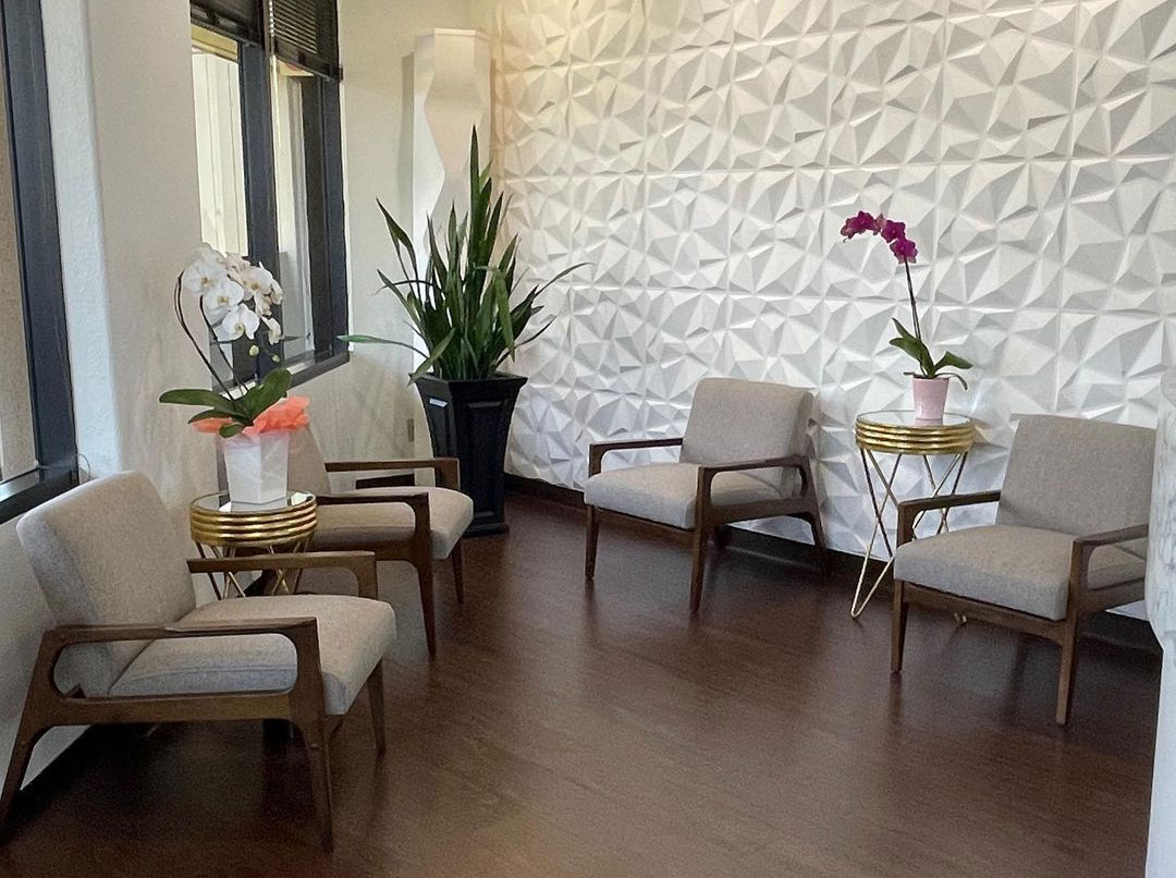 An image of an interior space, likely a waiting area or lobby, with modern furniture and decorative elements such as a wall-mounted sculpture, a potted plant, and a vase with flowers.