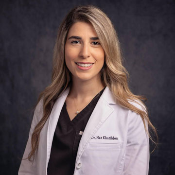 A woman in a white lab coat, smiling at the camera.