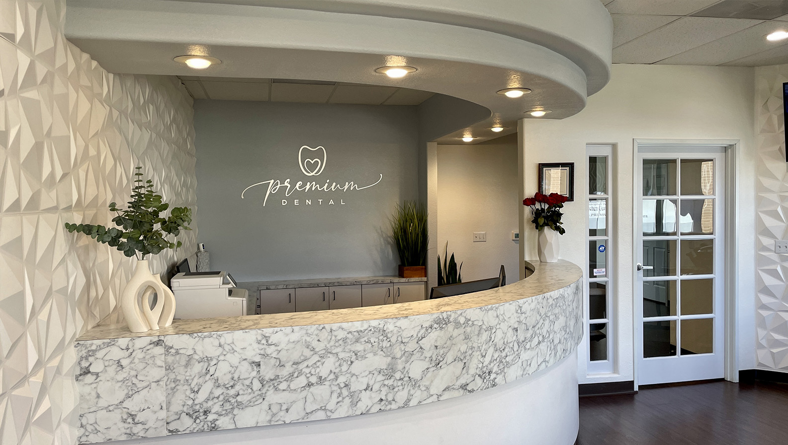 The image shows an interior view of a dental office reception area, featuring a modern design with marble countertops and a sign that reads  Premier Dental.