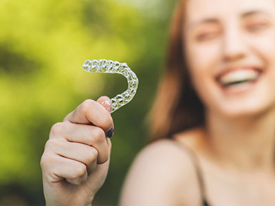 A person is holding up a clear plastic toothbrush with bristles, smiling at the camera.